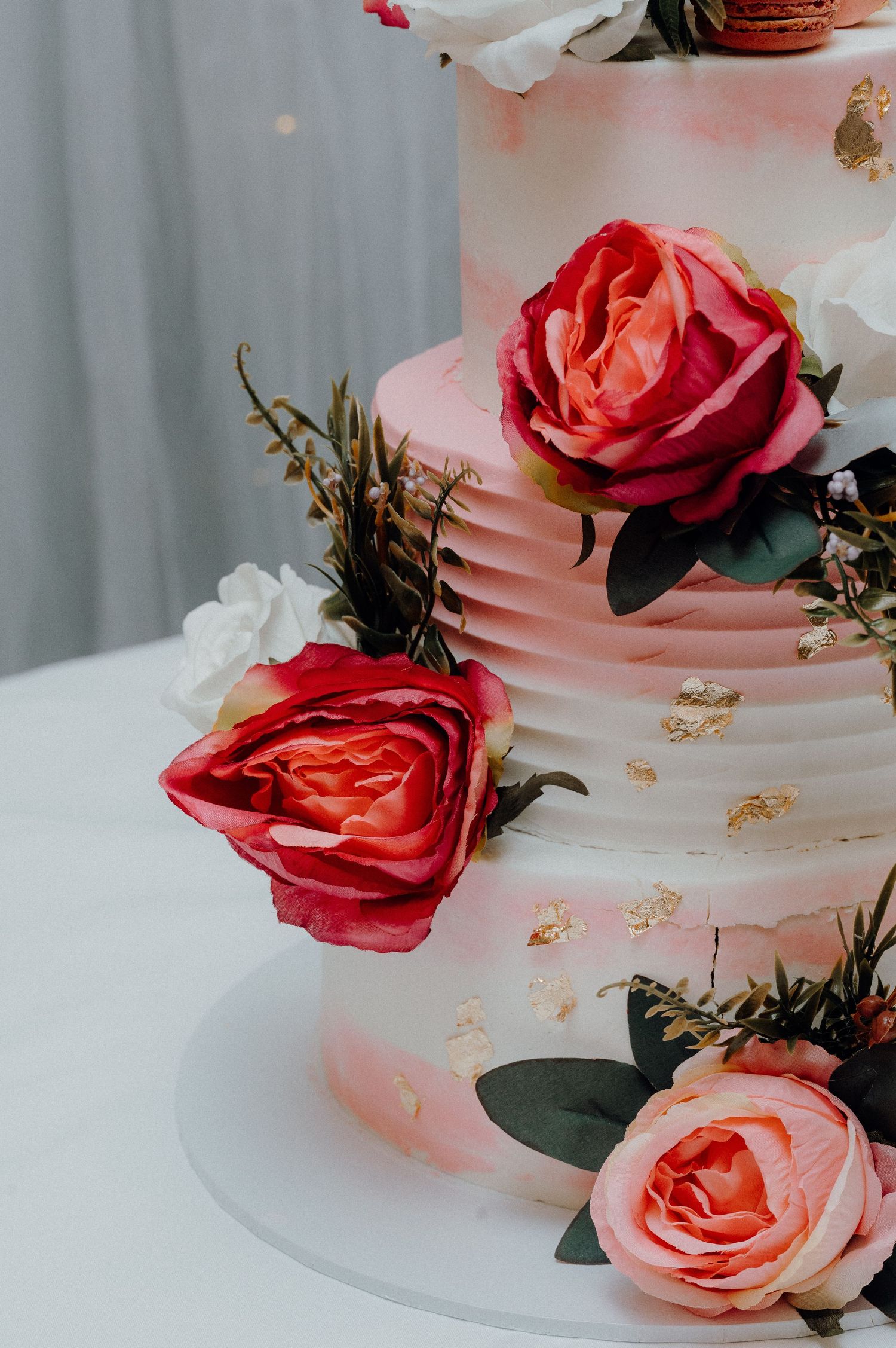 Close-up of wedding cake tiers adorned with realistic sugar roses in coral and red hues.