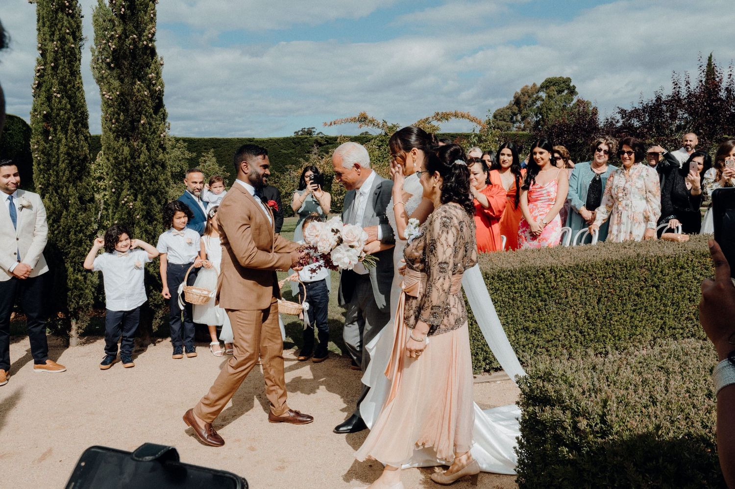 Wedding celebration on a garden path with guests gathered around during an outdoor ceremony.