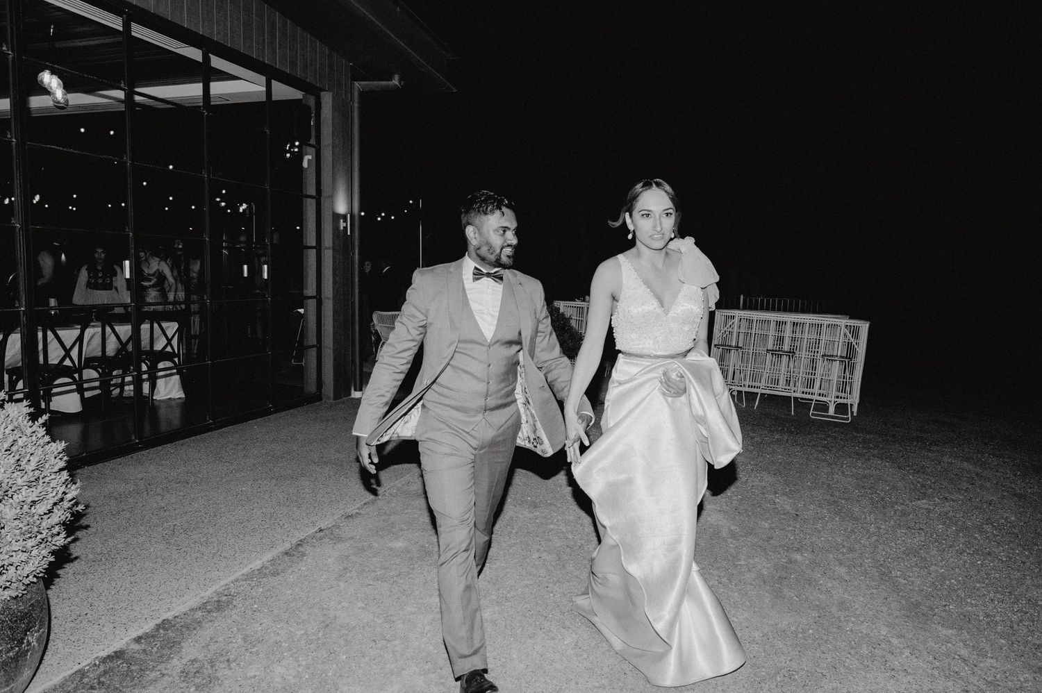 Bride and groom walking hand in hand at night after their wedding celebration.