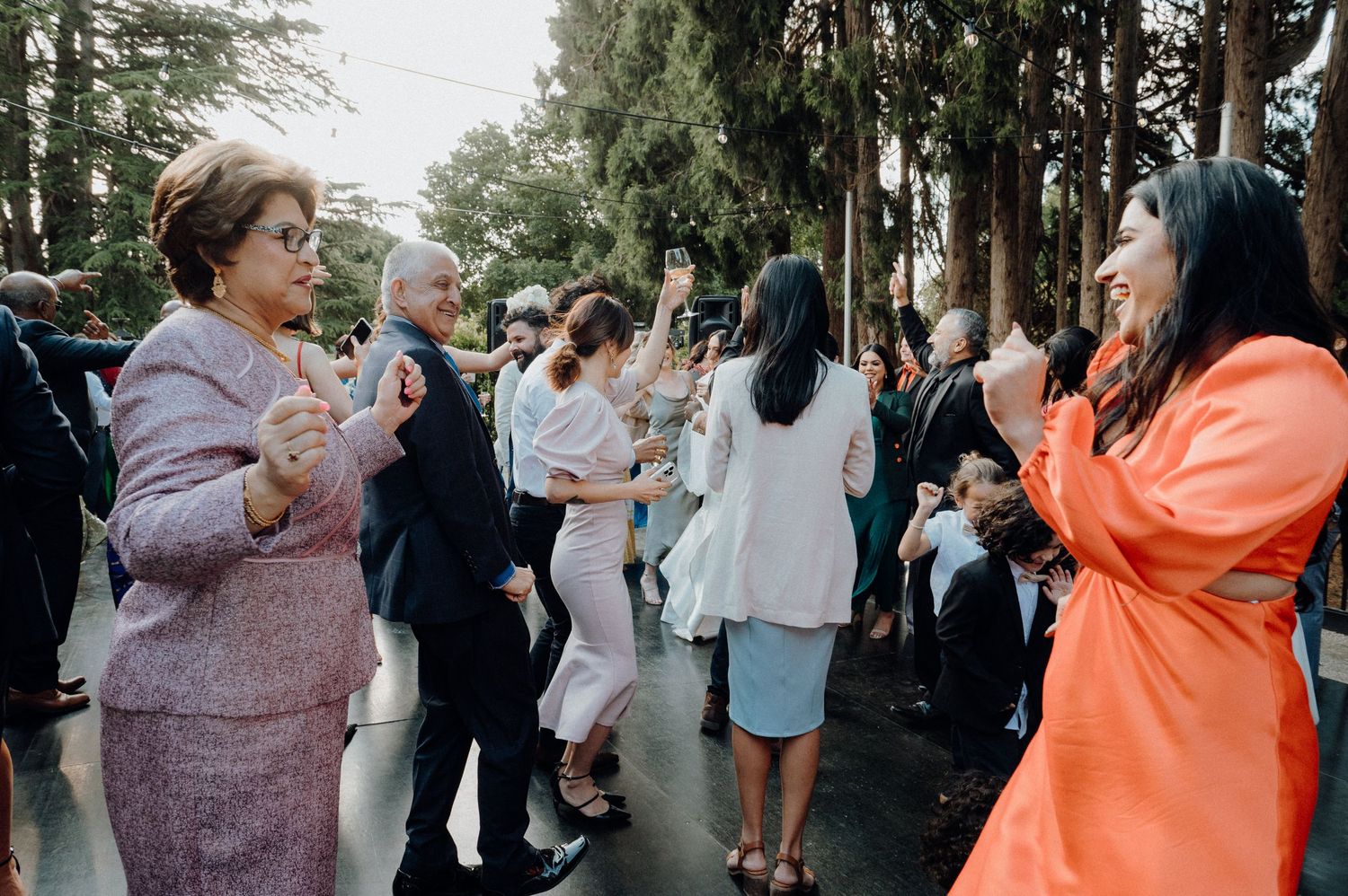 Wedding reception guests dancing and celebrating in formal attire outdoors.