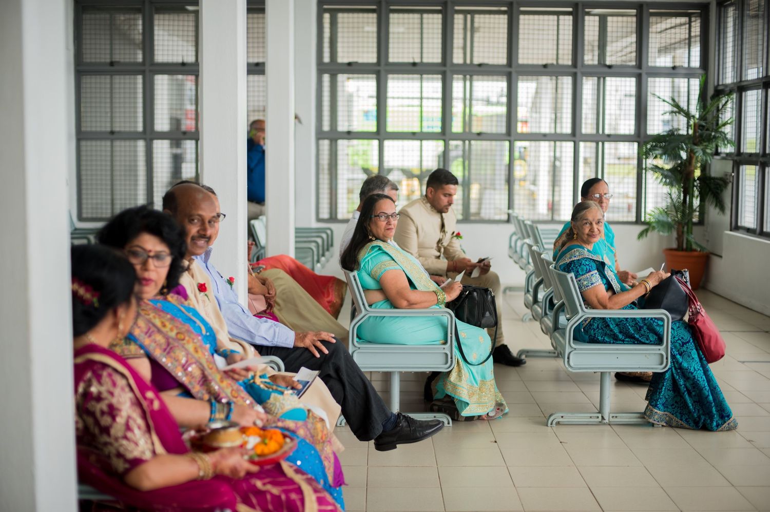 Wedding guests seated in a modern waiting area wearing traditional Indian formal wear.