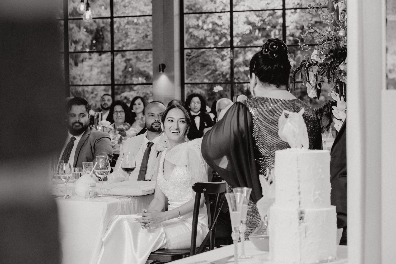 Black and white candid shot of wedding reception guests enjoying speeches.