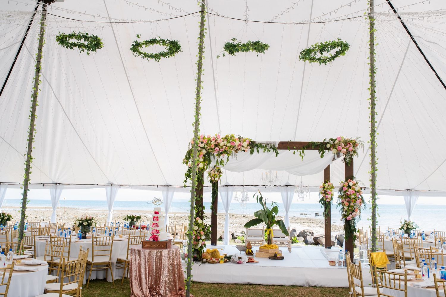 Elegantly decorated wedding tent interior with floral arrangements and hanging greenery wreaths.