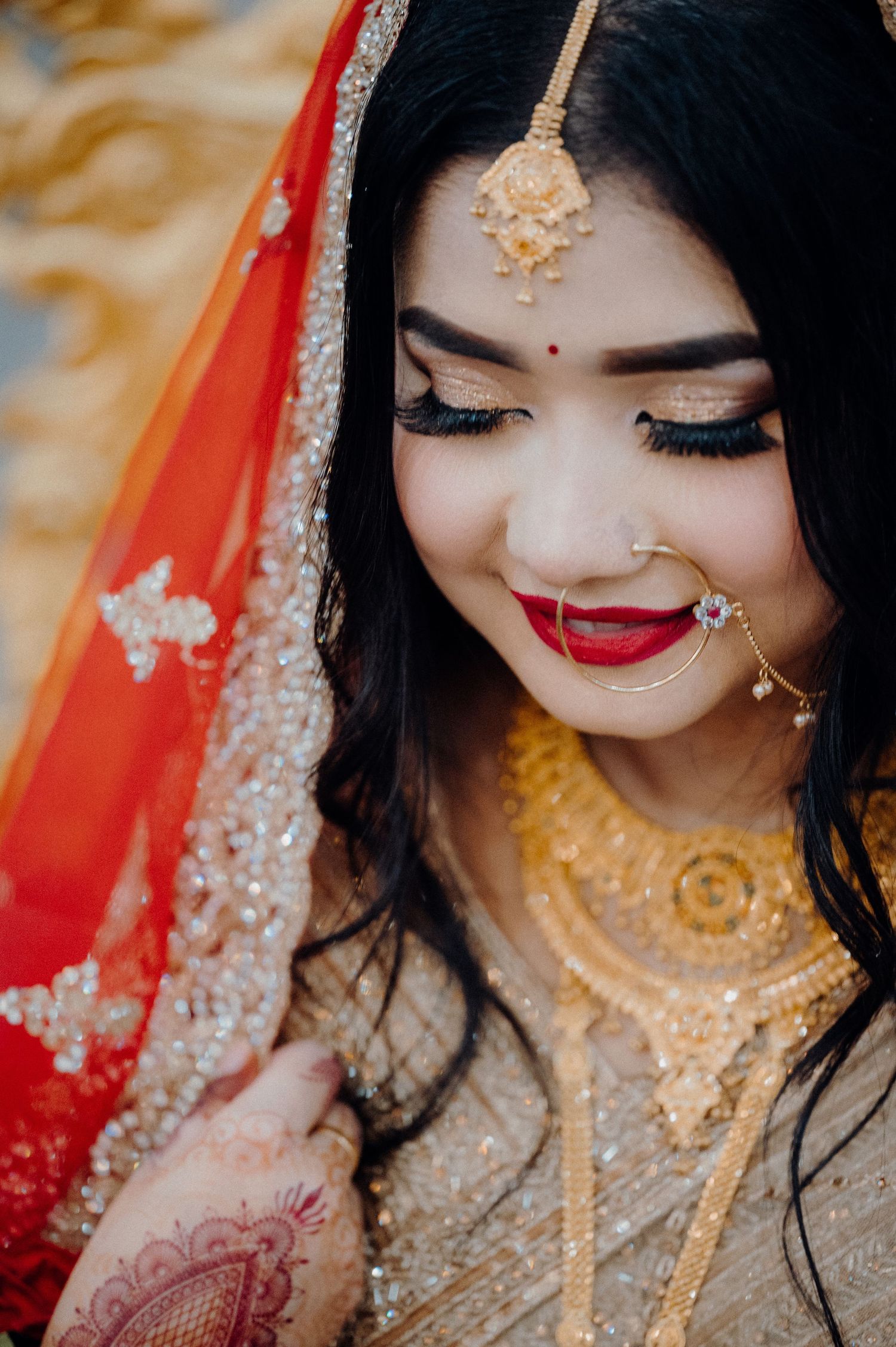 Close-up portrait showcasing traditional South Asian bridal jewelry and makeup with a red and gold dupatta.