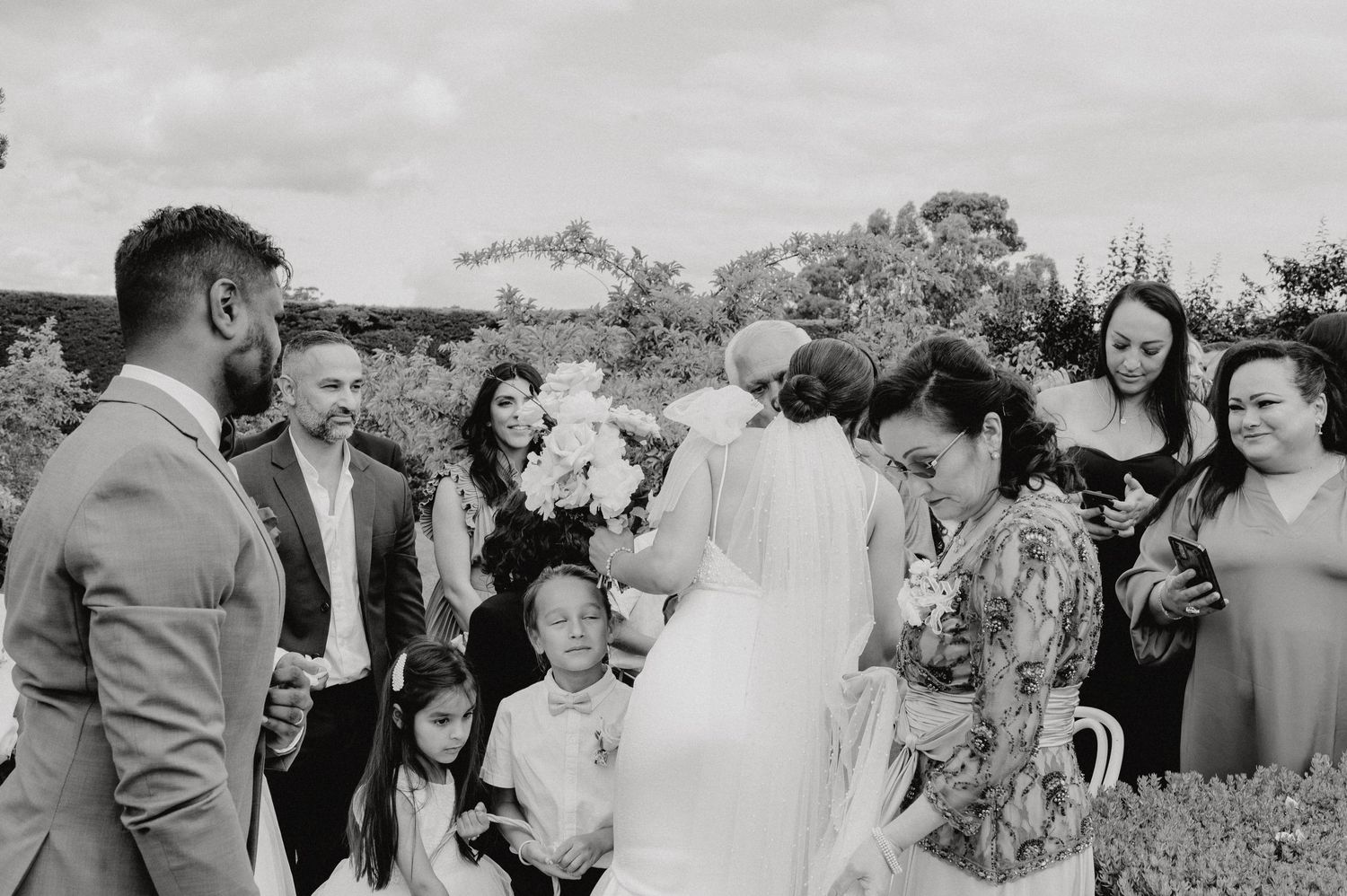 Black and white photo of wedding celebration with guests gathered outdoors.