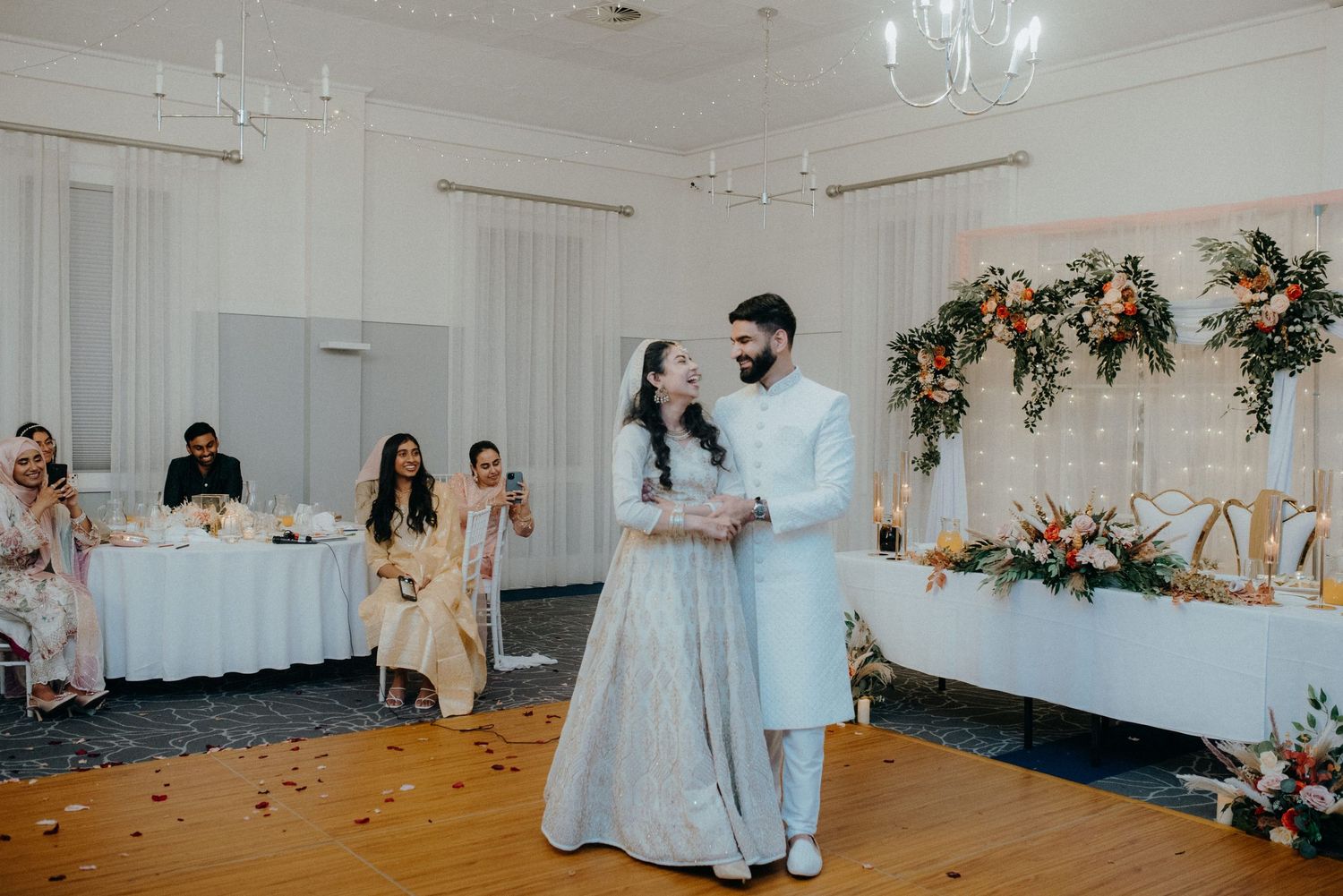Couple sharing their first dance in a beautifully decorated reception hall with floral arrangements.