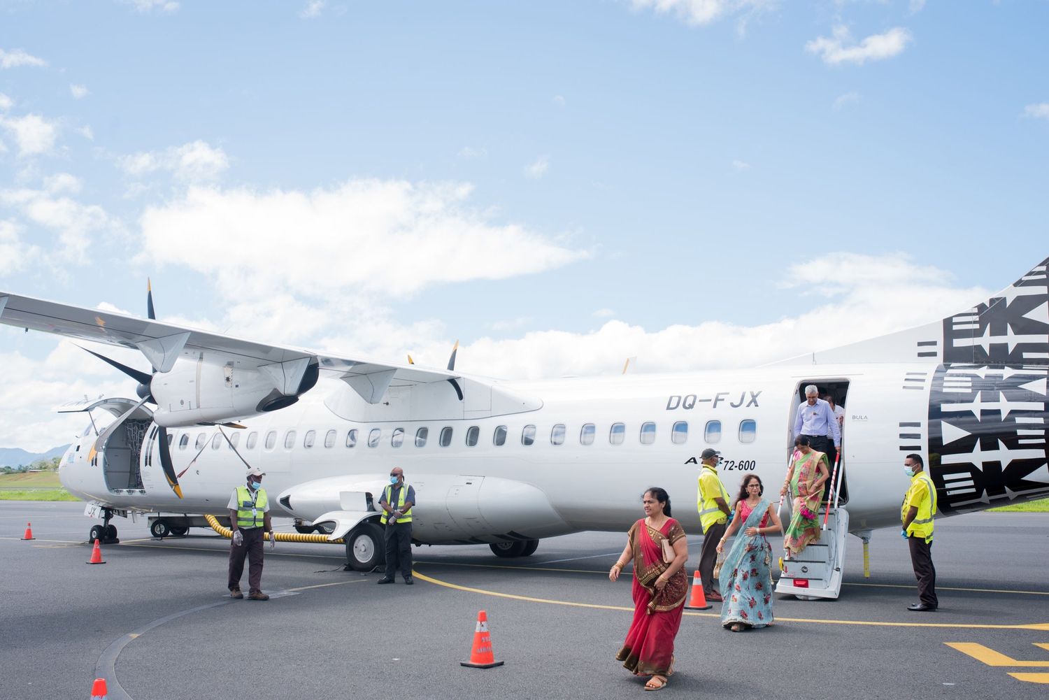 Passengers in vibrant cultural dress board a small propeller aircraft on sunny tarmac.