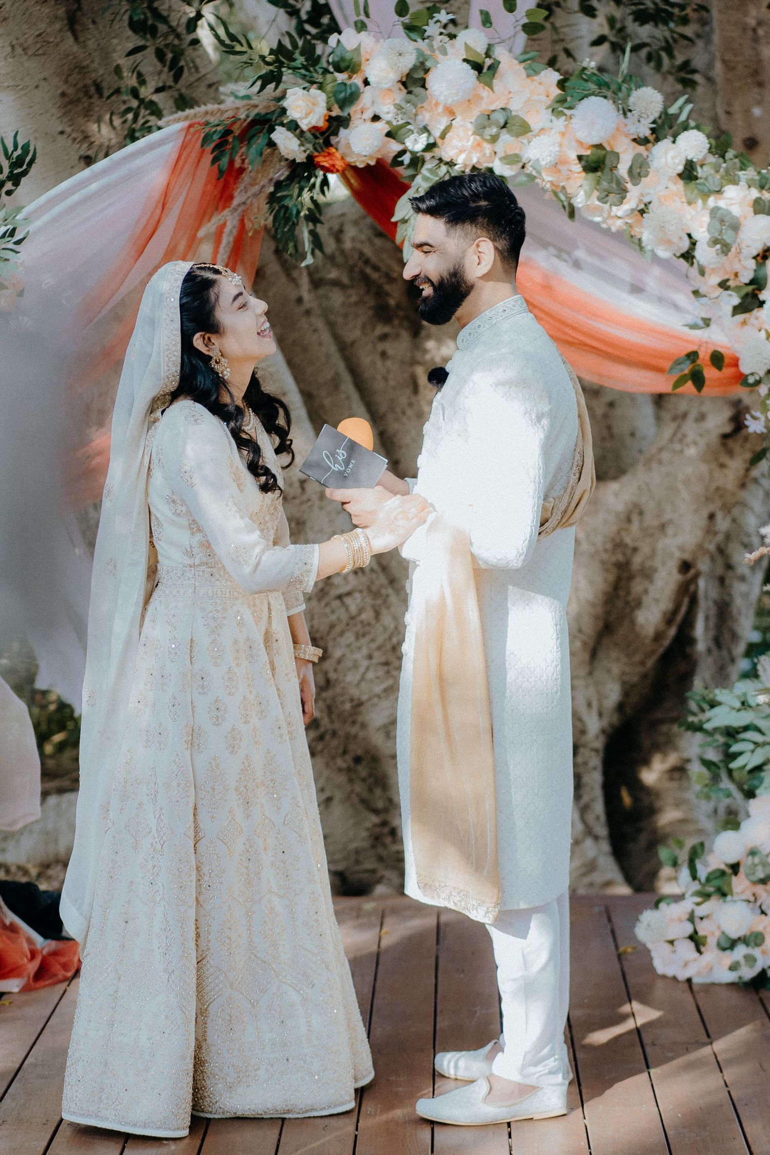 Couple shares a tender moment during their wedding ceremony under a floral-decorated arch.