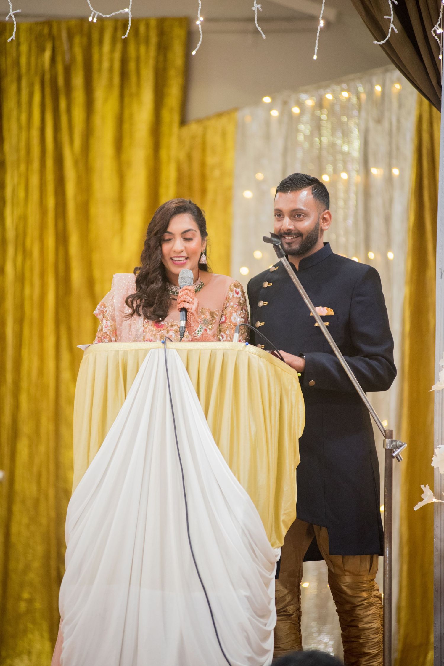 Couple speaking at decorated podium with gold and white draping.