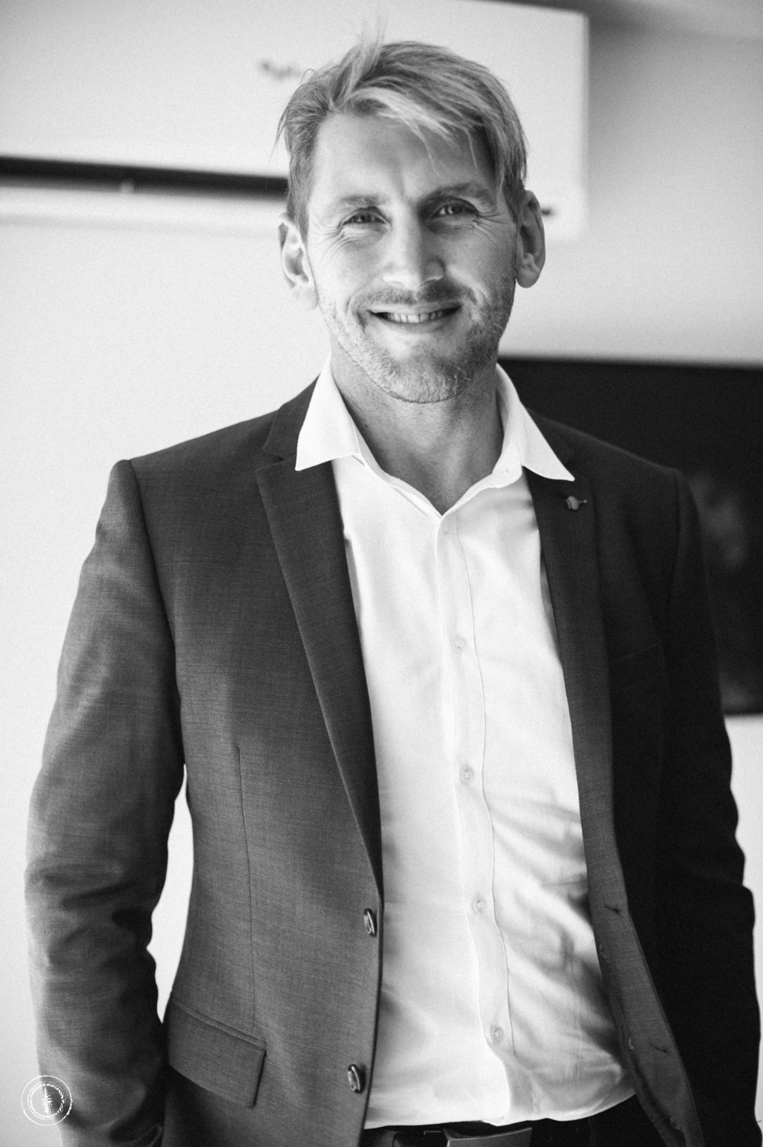 Professional black and white portrait of a businessman in a suit and white shirt smiling at camera.