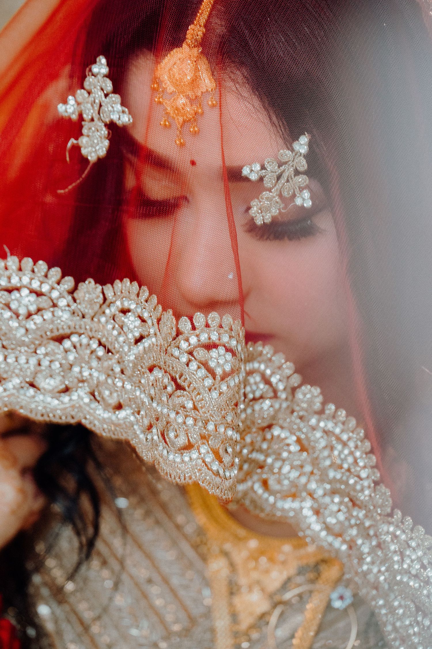 Traditional South Asian bridal jewelry and veil details with intricate beadwork and embellishments in red and gold tones.