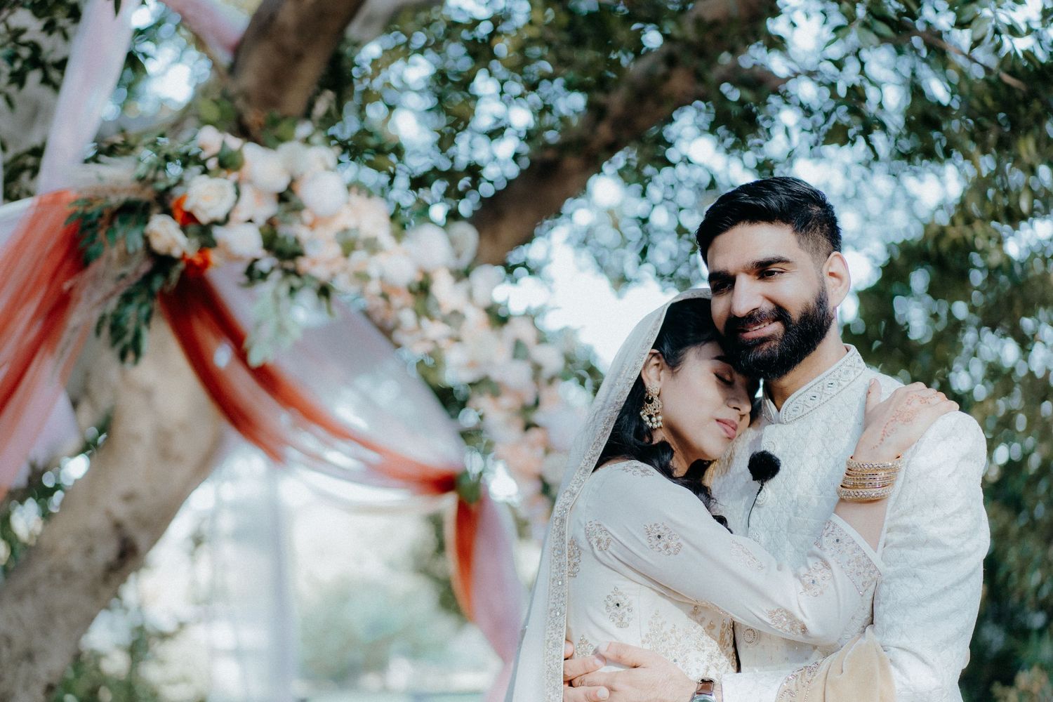 Candid wedding moment captured under floral arch with coral draping.