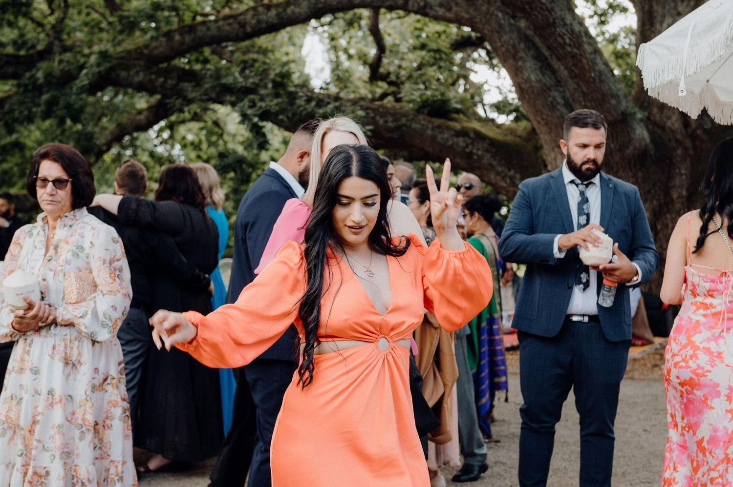 Wedding guests mingling under a large tree during an outdoor reception.