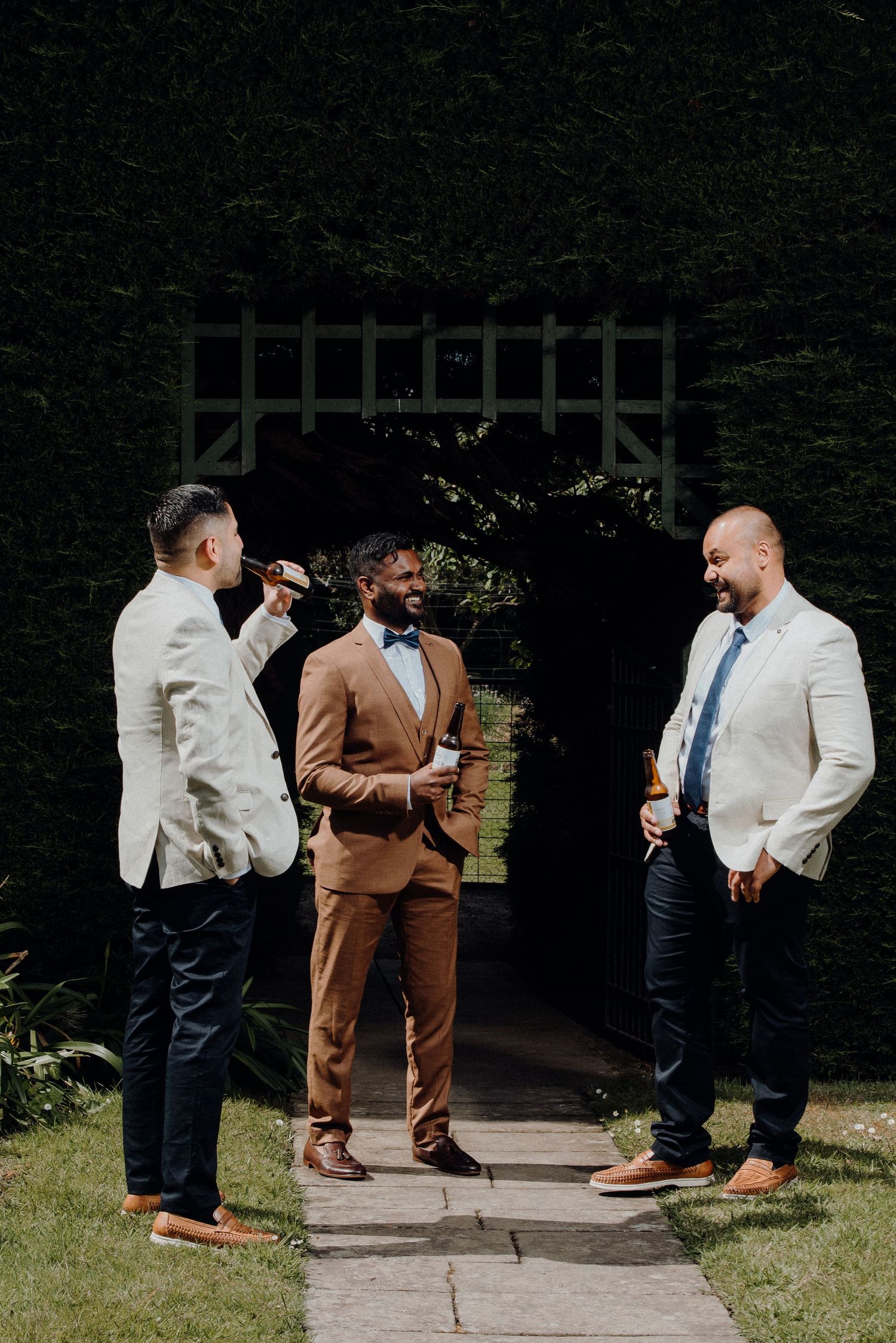 Three well-dressed attendees in suits socializing at an outdoor garden venue.