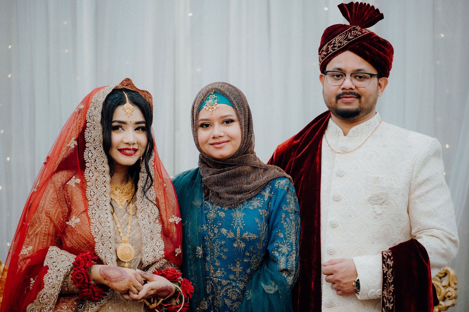 Wedding party members pose in traditional South Asian formal wear with ornate decorative details.