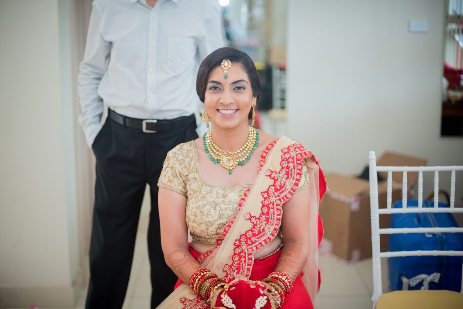 A woman in a traditional red and gold saree sits elegantly at a wedding celebration.