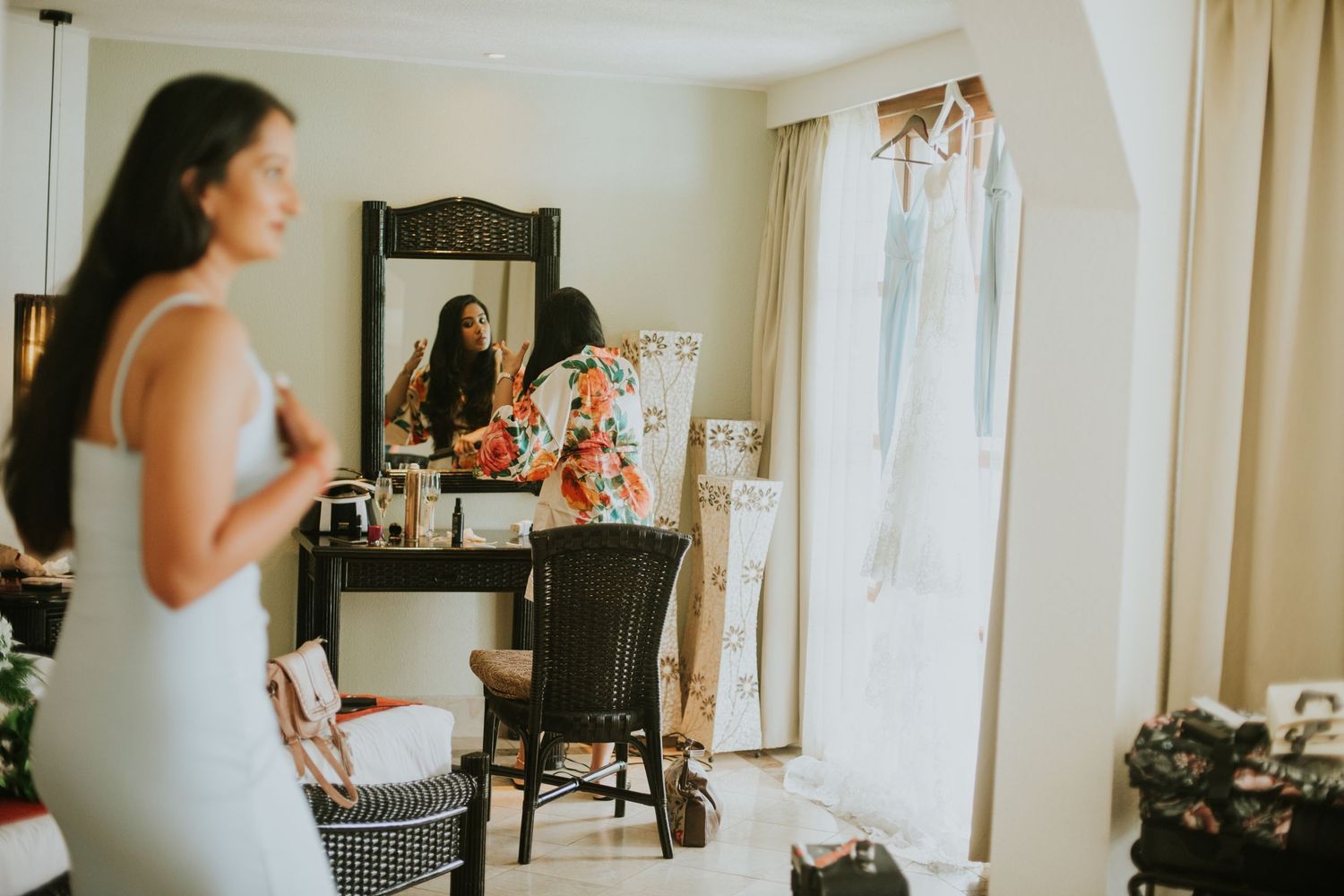 Bride getting ready in front of a vanity mirror in a sunlit room with white decor.