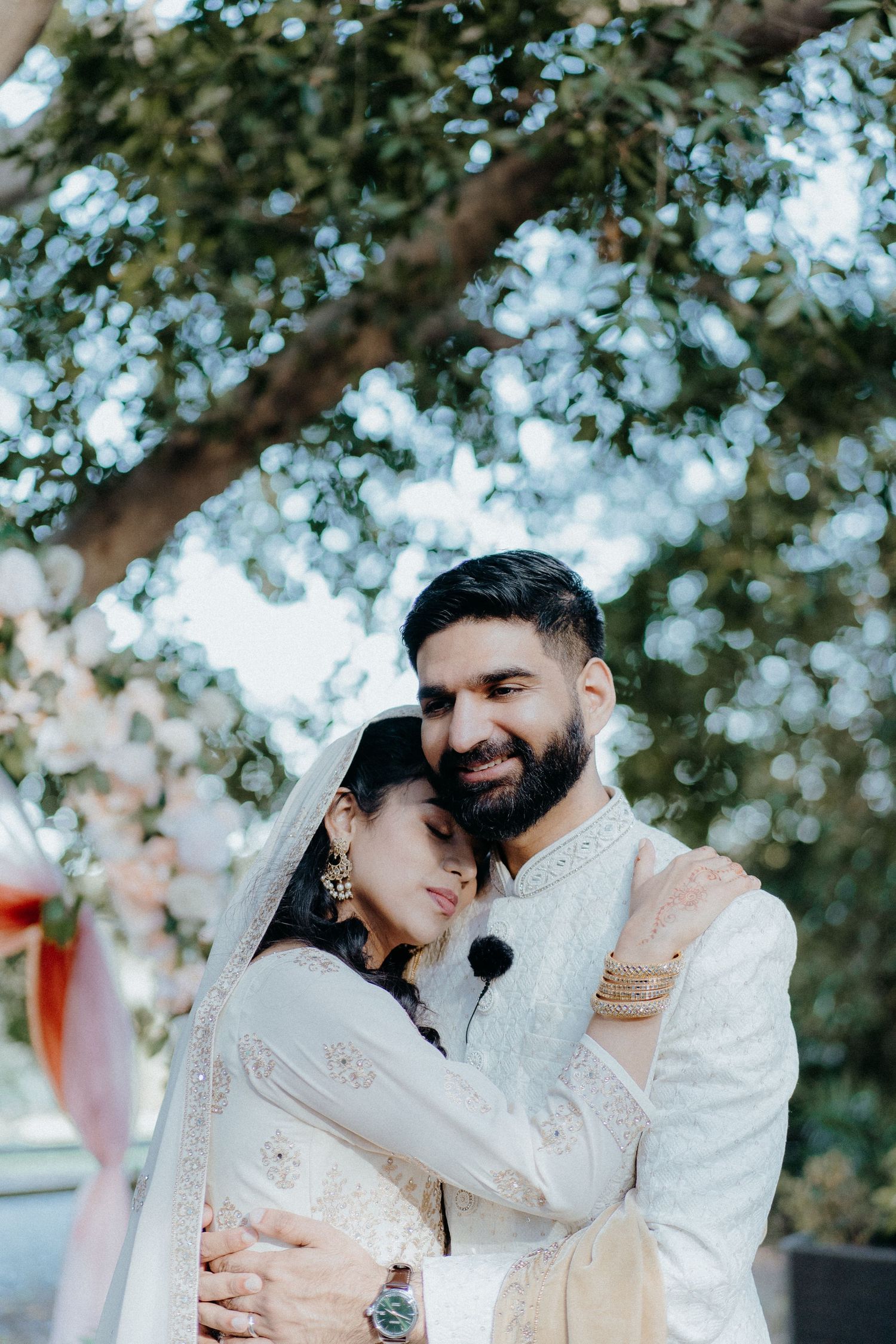 Romantic embrace during outdoor wedding photoshoot with dreamy tree backdrop.