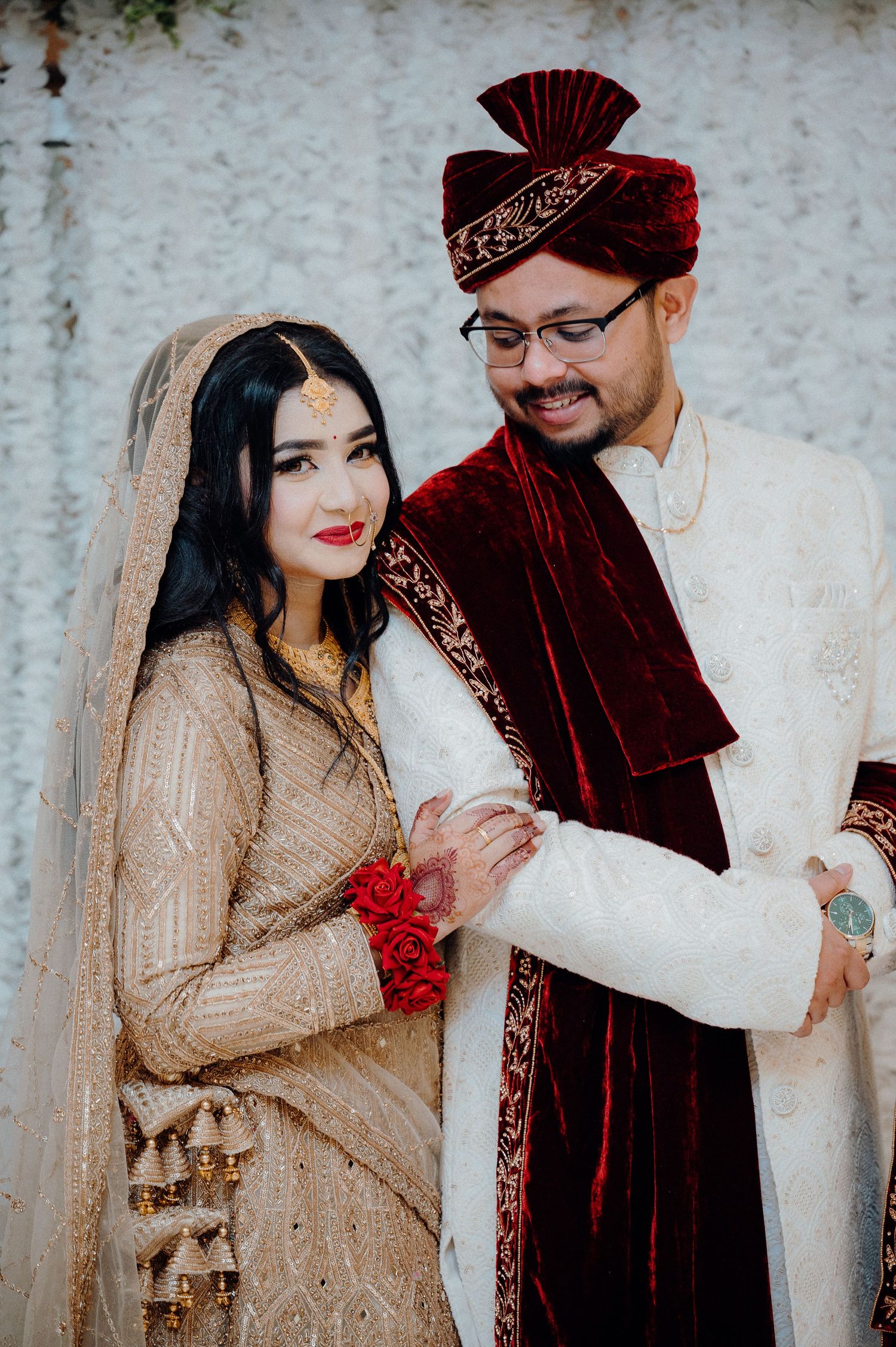 Wedding couple in traditional attire sharing intimate moment against white backdrop.