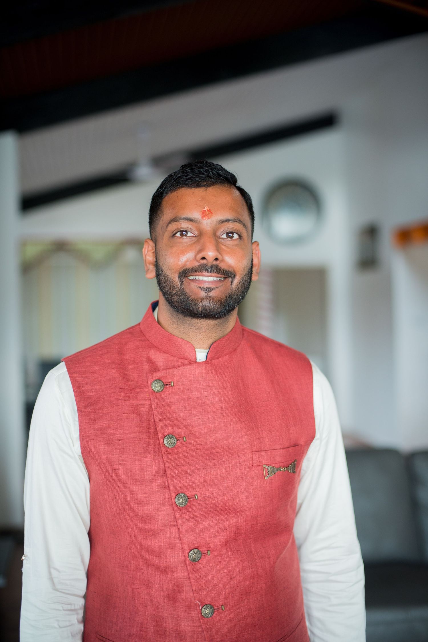 Person in traditional red nehru jacket and white kurta smiling warmly at camera.