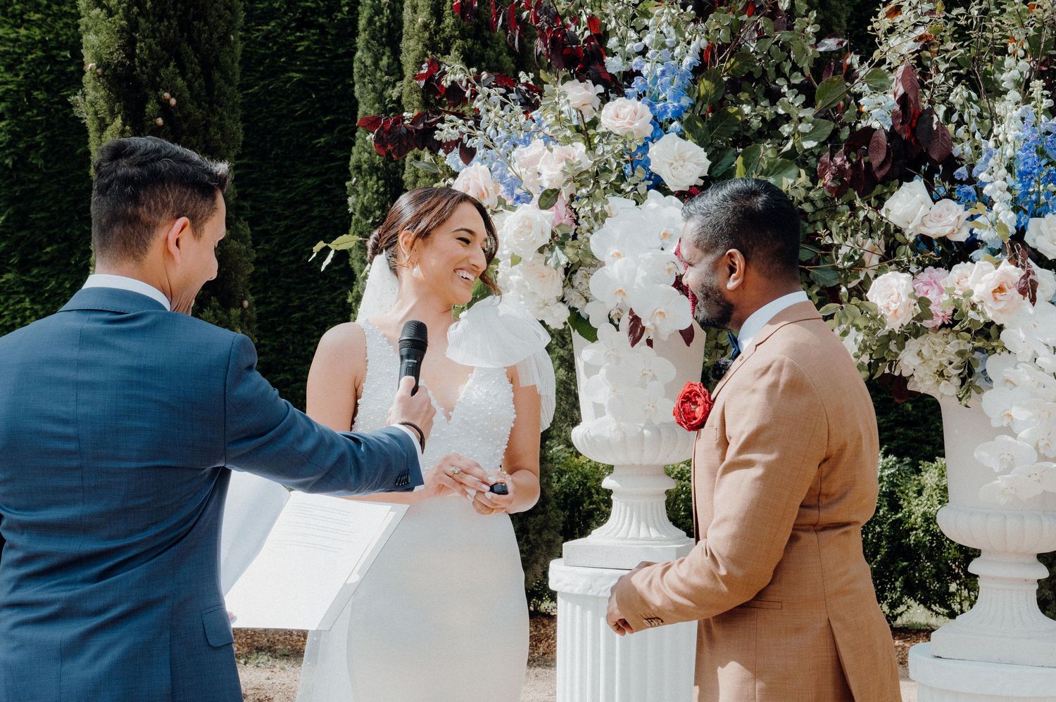 Wedding ceremony exchange under an ornate floral arch with white and blue flowers.