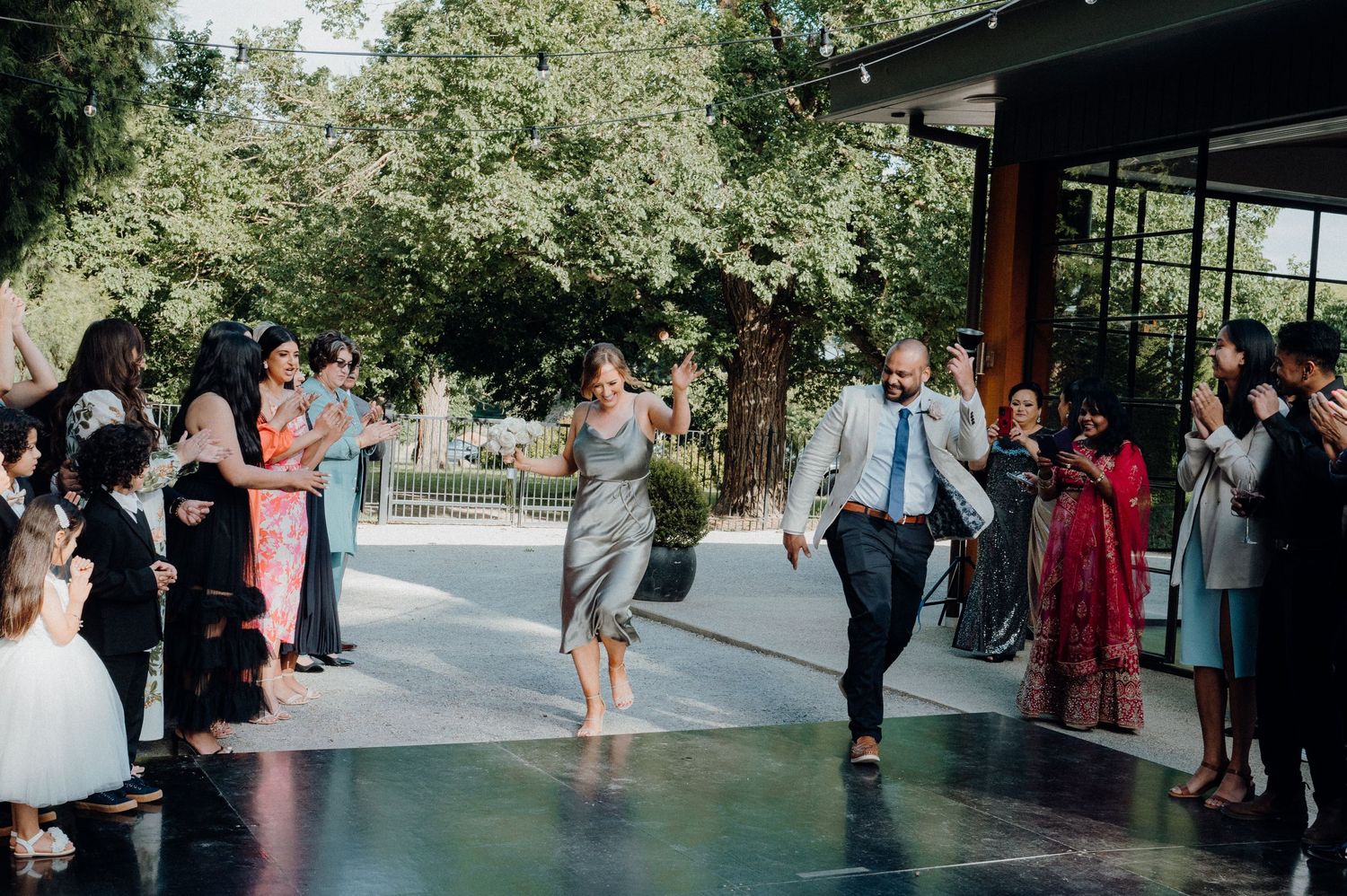 Wedding guests dancing enthusiastically on black dance floor at outdoor venue.