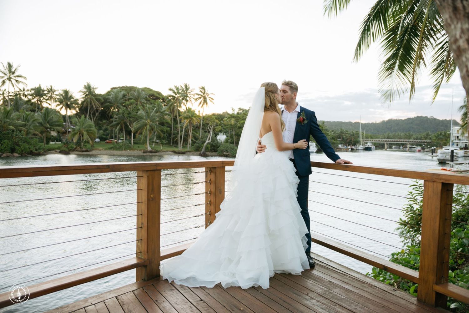 Romantic wedding portrait on a wooden deck overlooking tropical waters and palm trees.