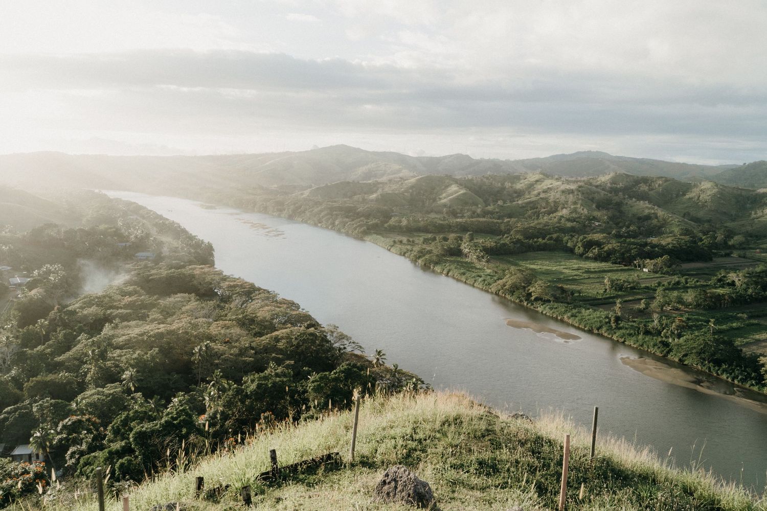 Aerial view of winding river through green hills during sunset.