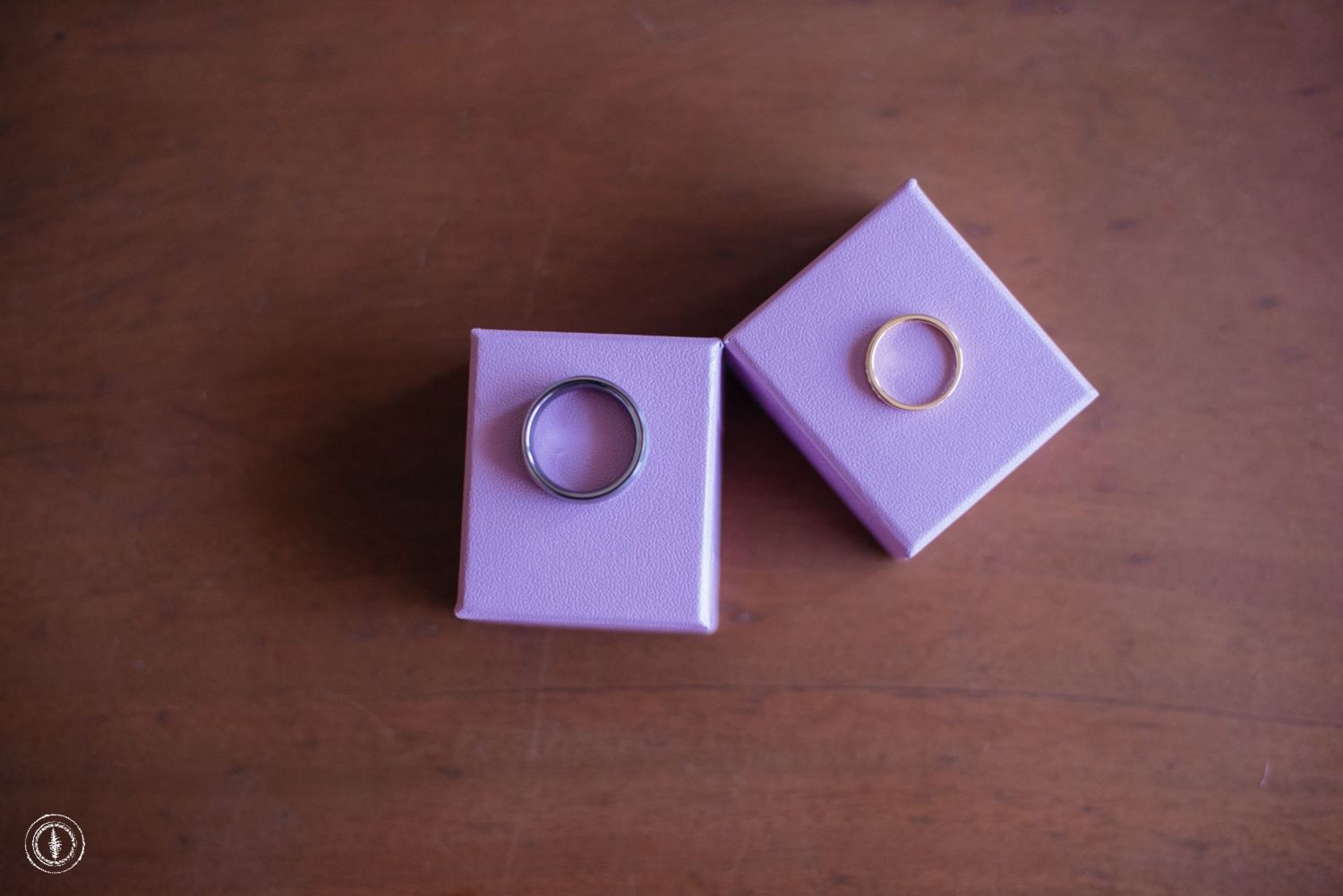 Two wedding rings displayed in purple jewelry boxes on wooden surface.