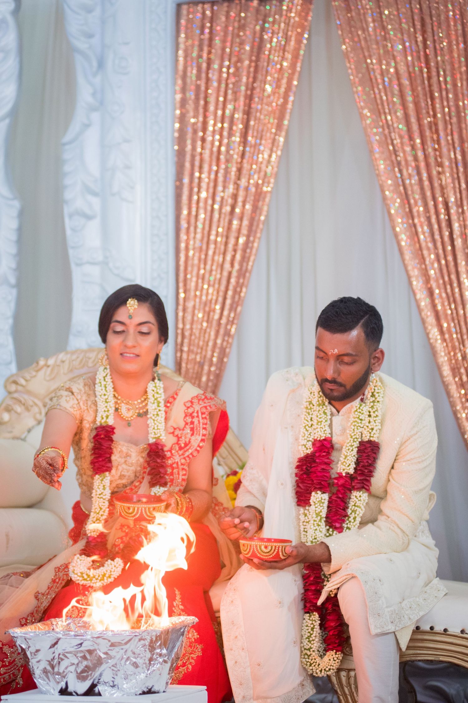 Wedding couple performing traditional fire ceremony with garlands and ceremonial items.