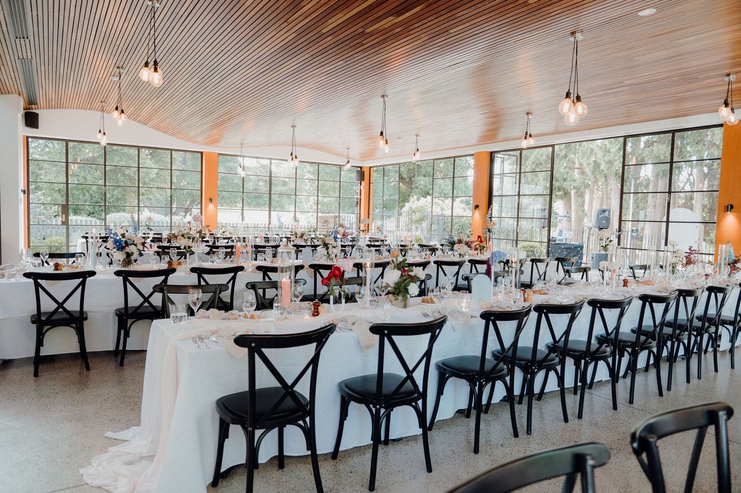 Modern wedding venue with black crossback chairs and large windows overlooking nature.