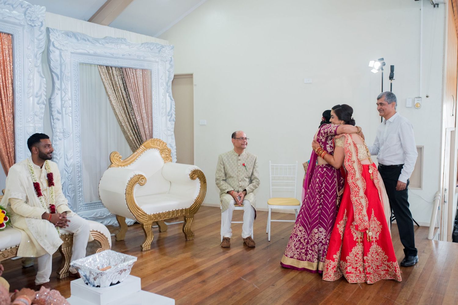 Traditional wedding ceremony with ornate white frames and peach curtains as backdrop.