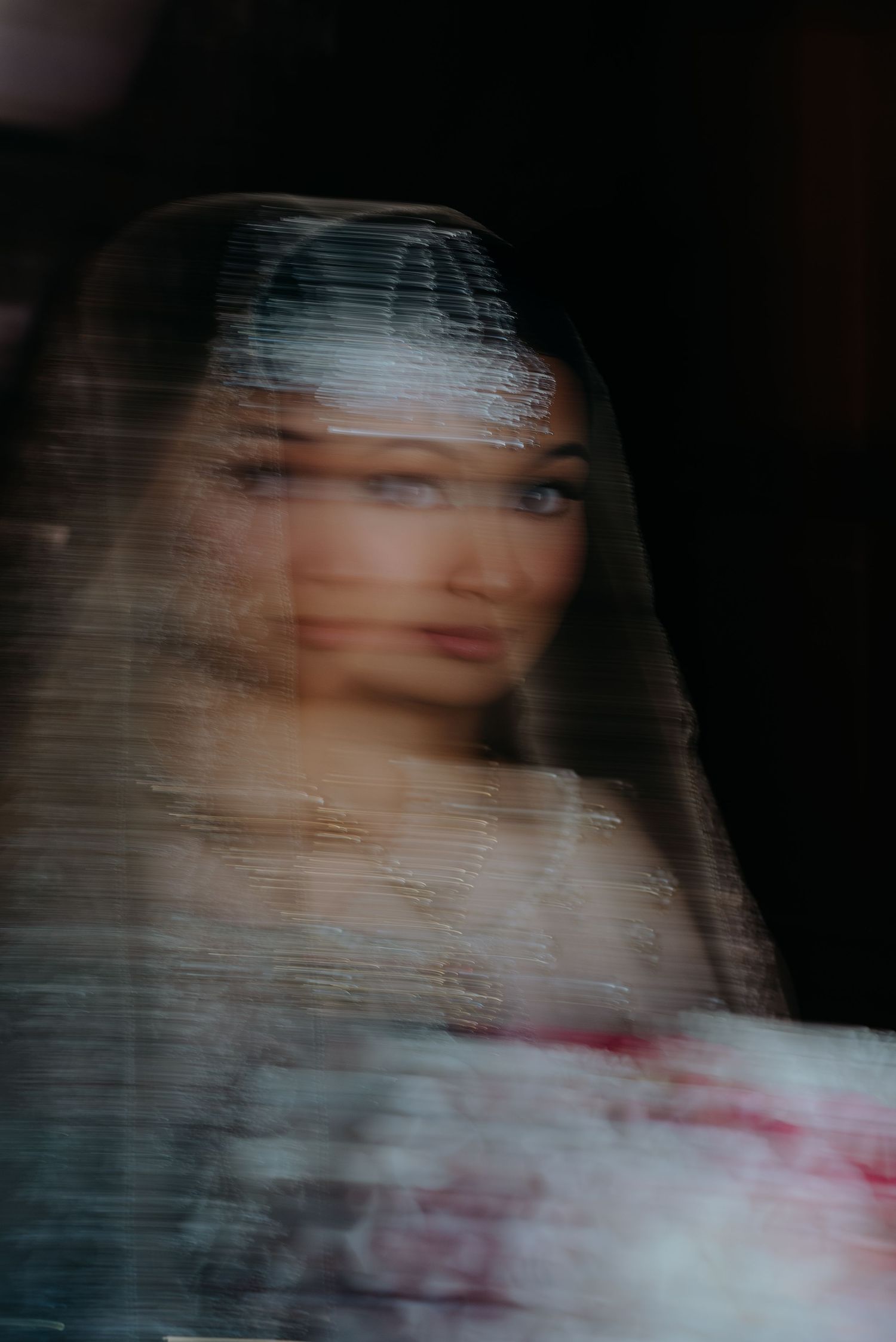 Dreamy blurred portrait of a bride wearing a veil, captured through a translucent surface.