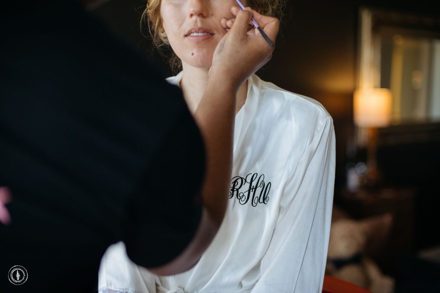 Close up of person having makeup applied while wearing monogrammed white robe.