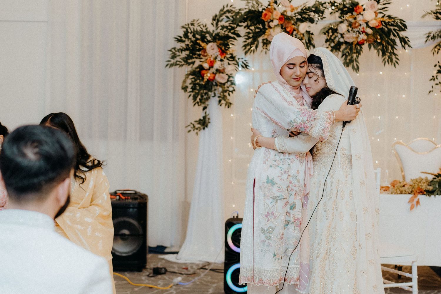 Wedding guest speaking into microphone with floral decorations and lights in background.