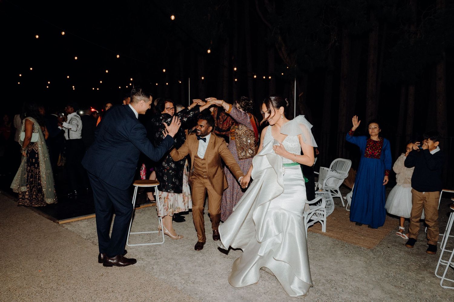 Wedding guests dancing together on the dance floor during an evening reception celebration.