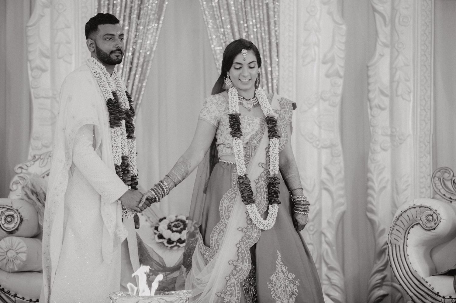 A black and white photograph capturing a traditional Indian wedding ceremony with decorative curtains.