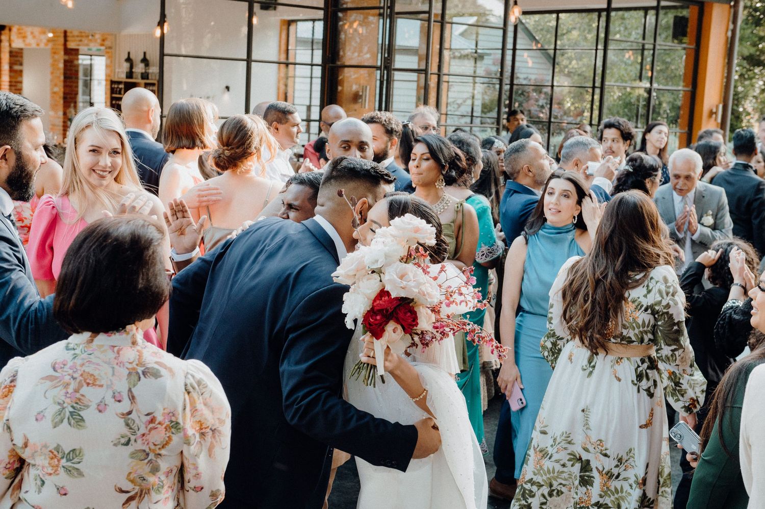 Crowded wedding reception with guests in colorful attire gathering around the newlyweds.