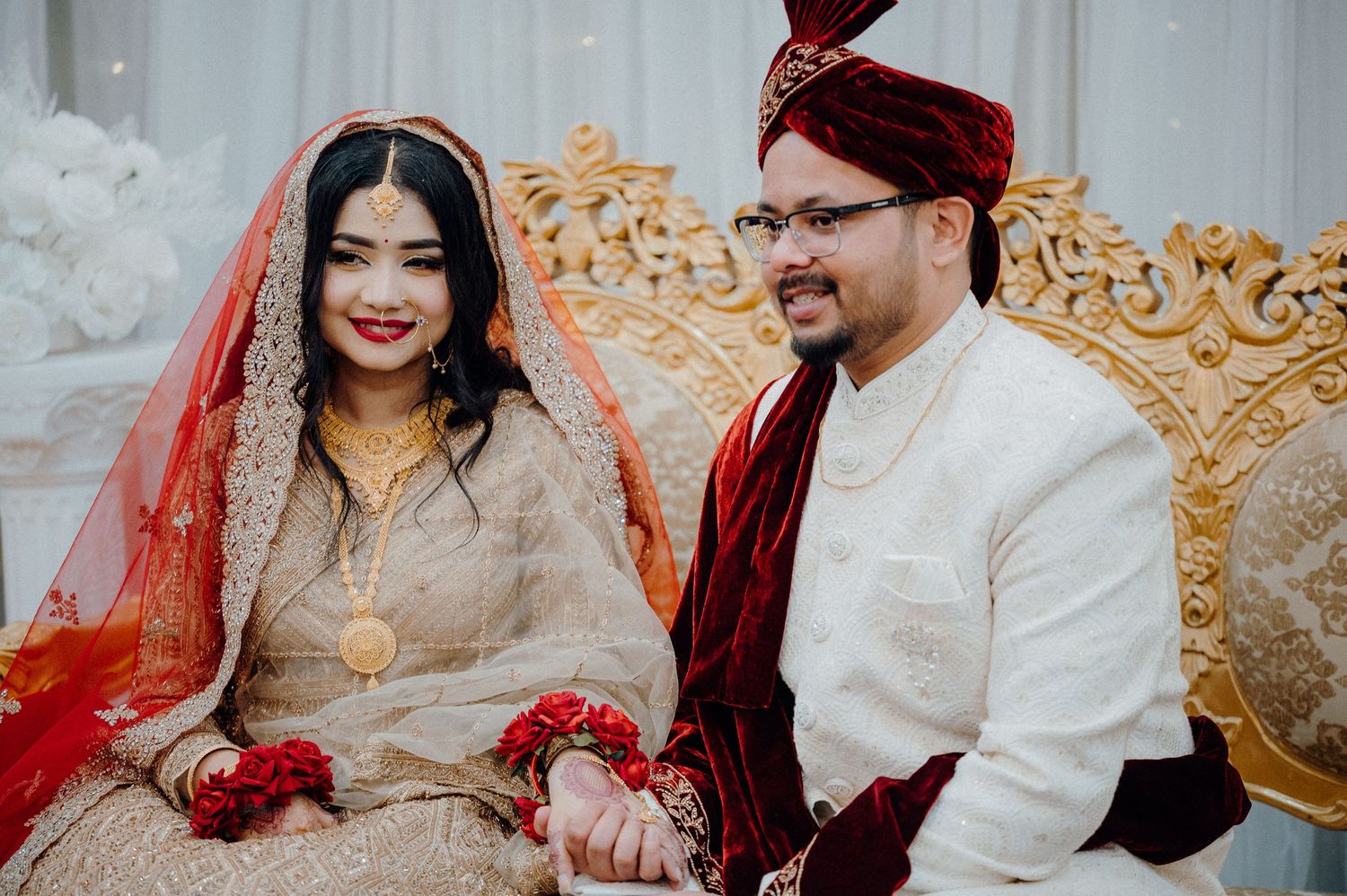 Newlyweds sitting together on ornate golden throne during traditional wedding ceremony.