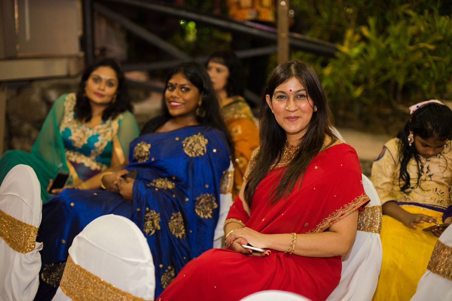Group wearing colorful traditional Indian attire seated at decorated outdoor event.