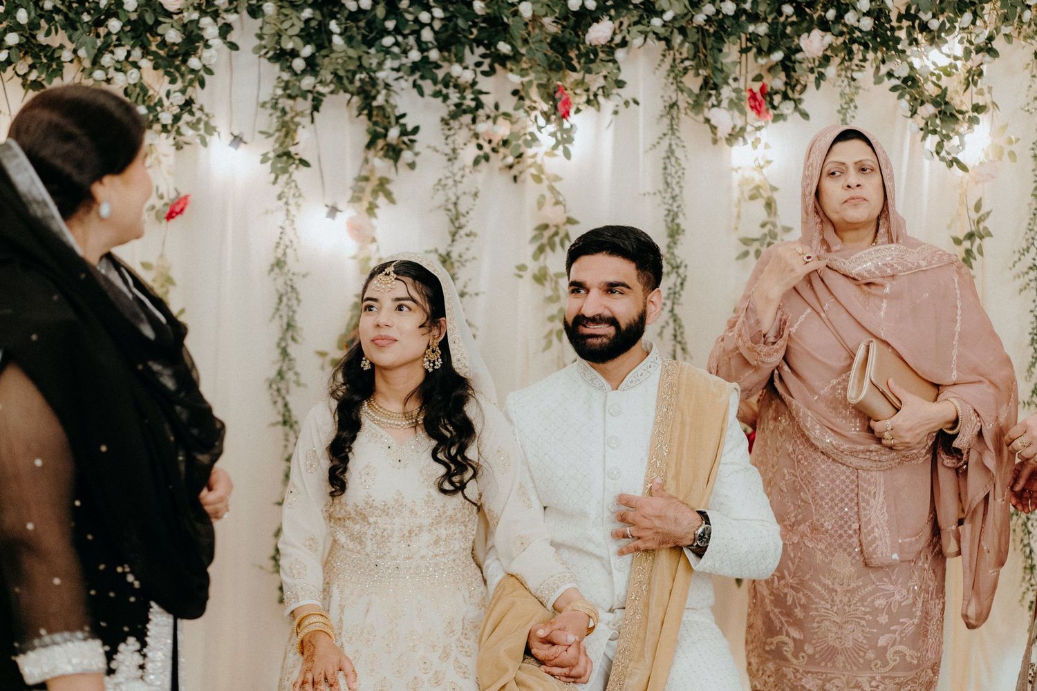 Traditional wedding ceremony with floral arch decorations and elegant attire in cream and peach tones.