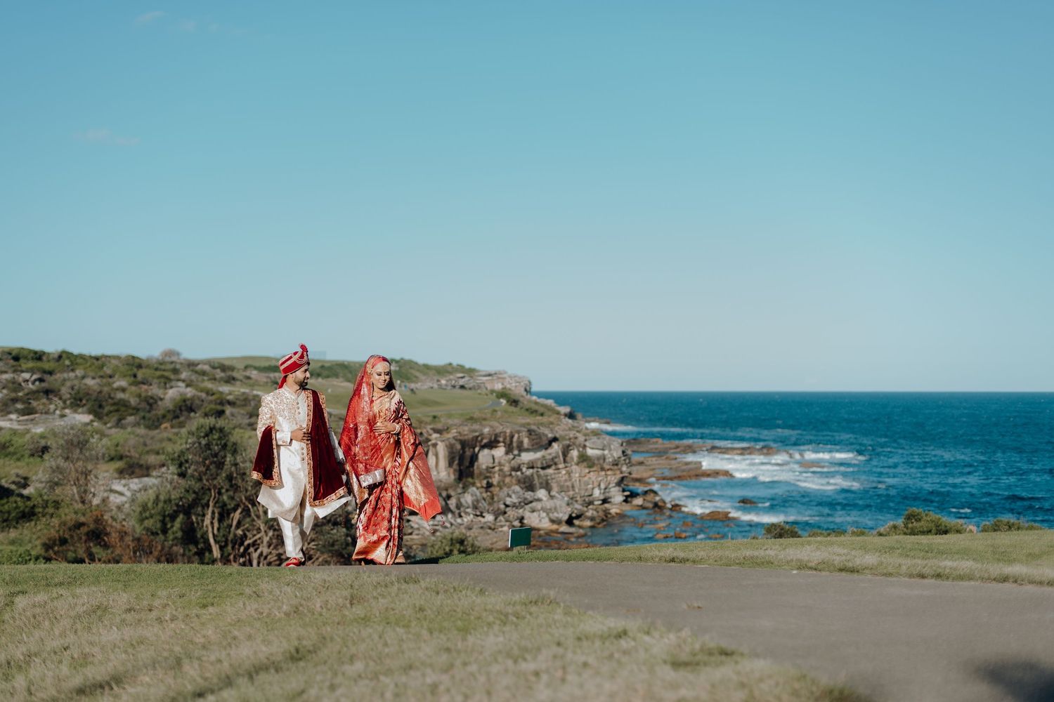 Couple walking on coastal cliffside path overlooking the ocean.