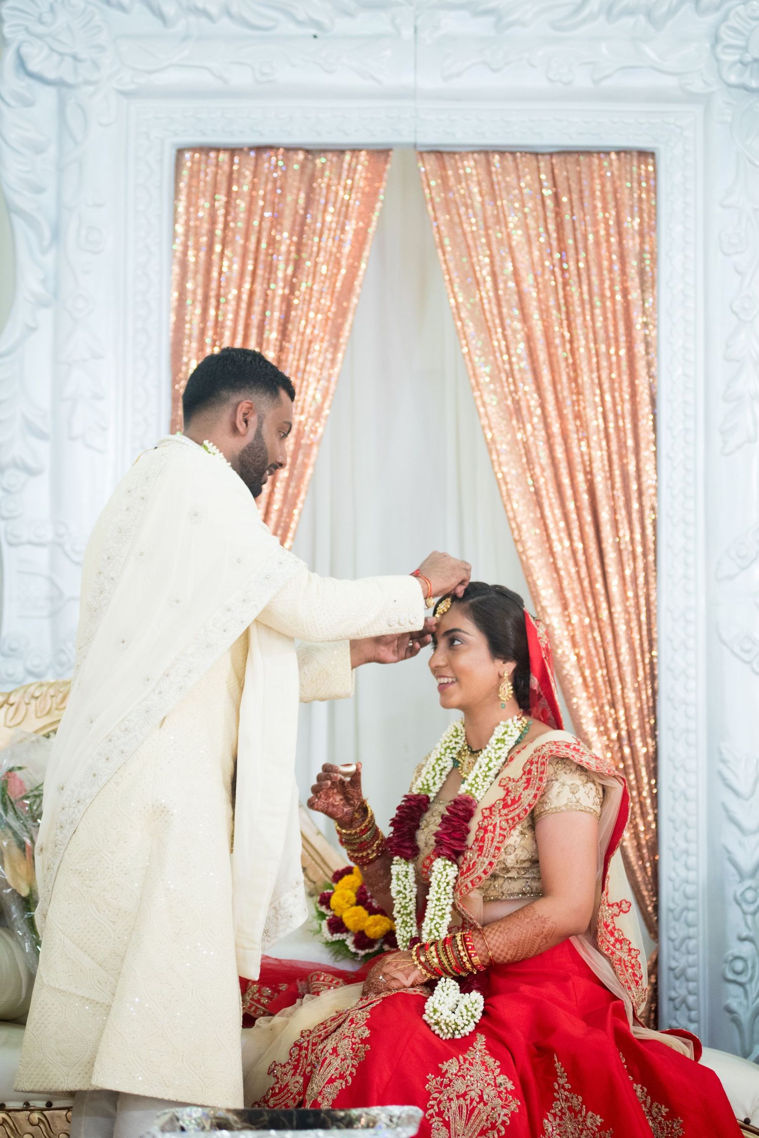 A traditional Indian wedding ritual with the groom placing sindoor on the bride's forehead.