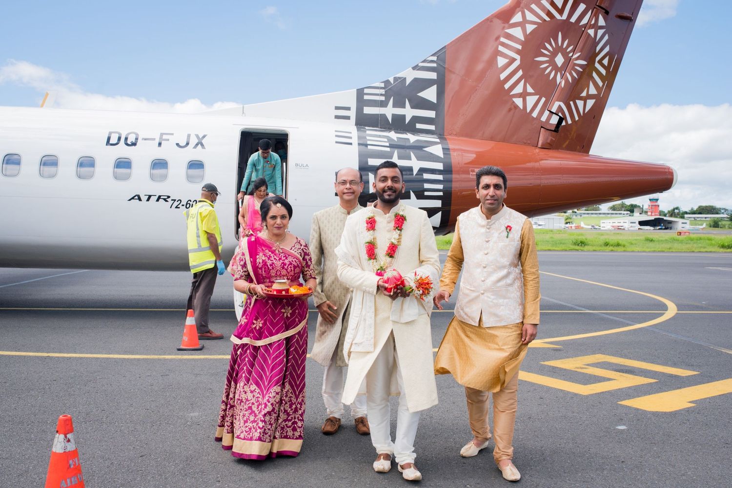 People in colorful traditional Indian clothing pose in front of a red and white aircraft on airport tarmac.