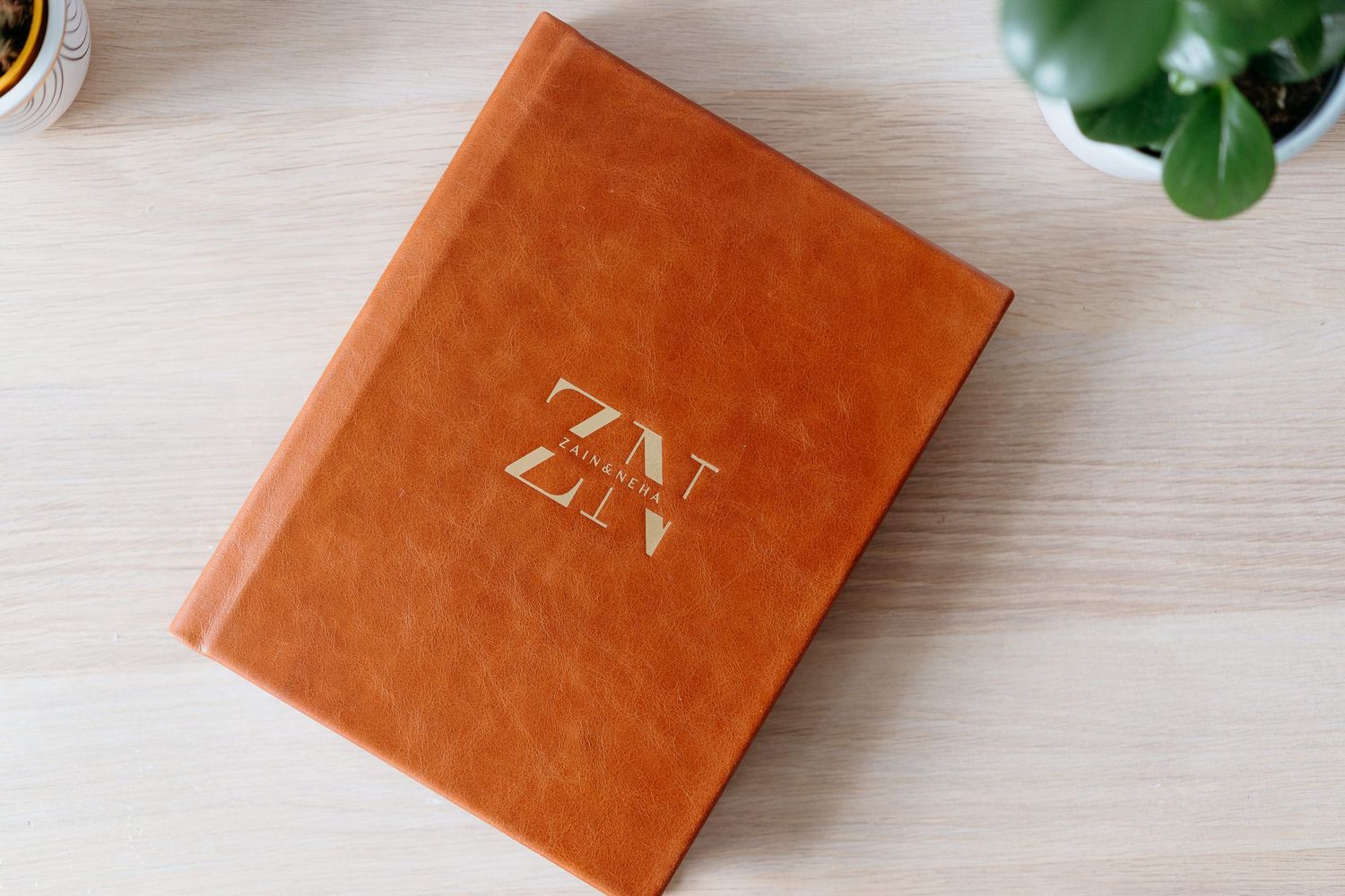 Brown leather wedding photo album with gold ZN monogram initials on wooden surface.