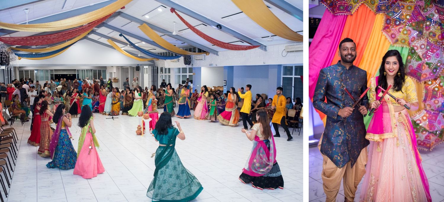 Large group celebration with people in colorful Indian attire dancing under draped fabric ceiling decorations.