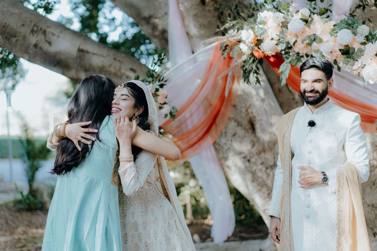 Wedding party sharing joyful moments during outdoor celebration under trees.