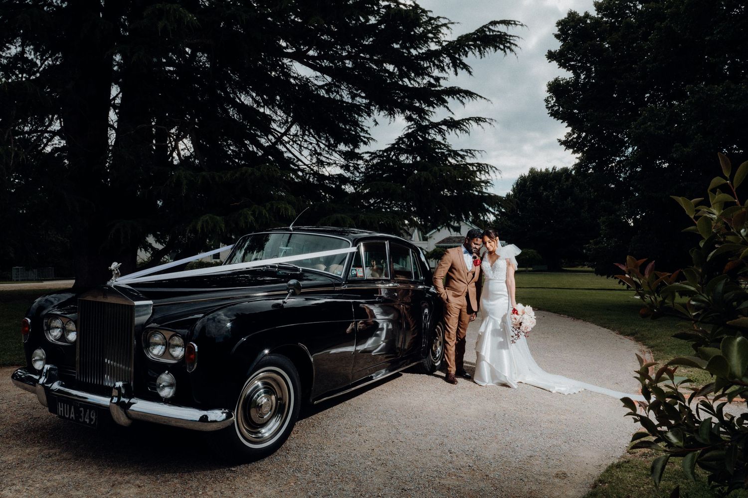 A vintage black Rolls Royce parked in a garden setting during a wedding photoshoot.