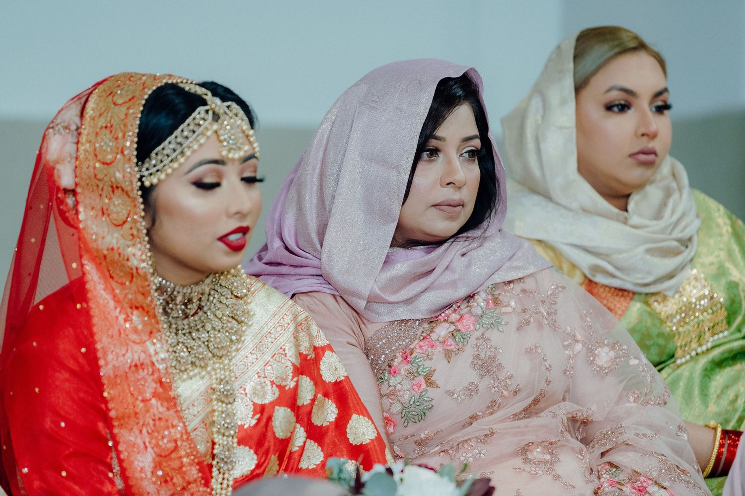 Three women wearing colorful traditional hijabs and formal attire sit together during a cultural celebration.