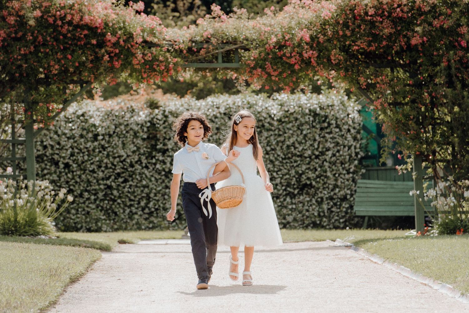 Two attendants walking along a garden path under a floral archway.